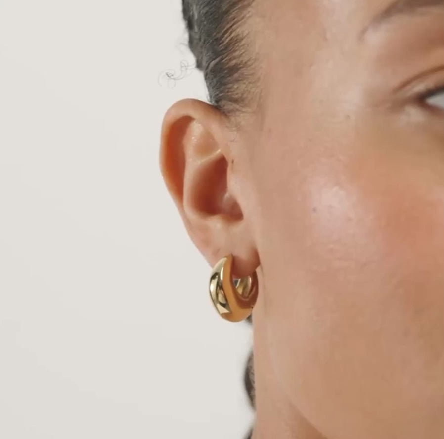 A close-up of a person's ear wearing a small polished gold hoop earring.