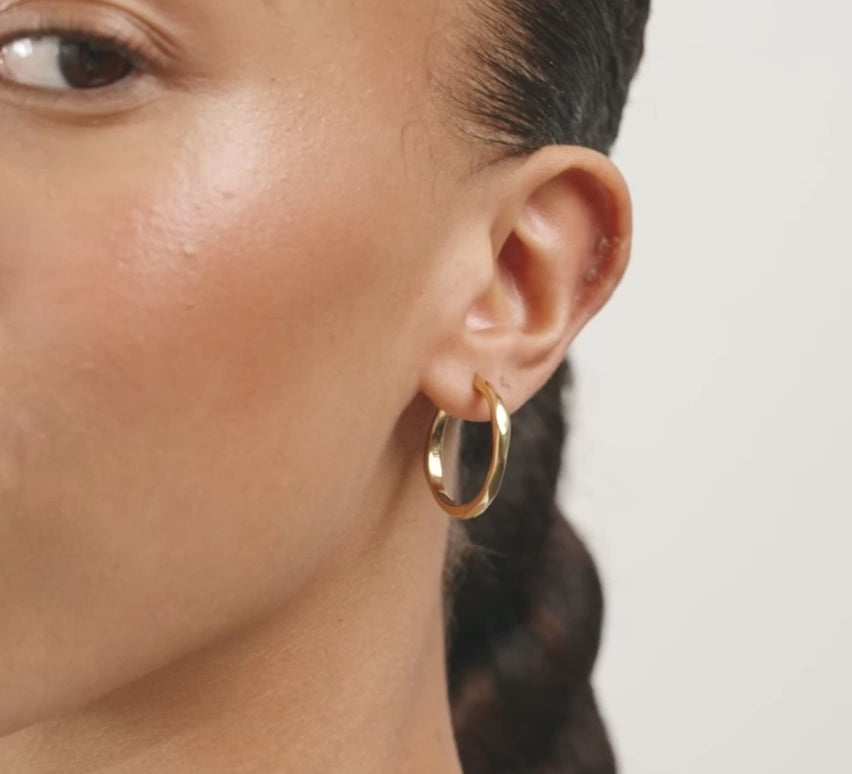 A close-up of a woman with dark curly hair wearing a thin gold hoop earring.