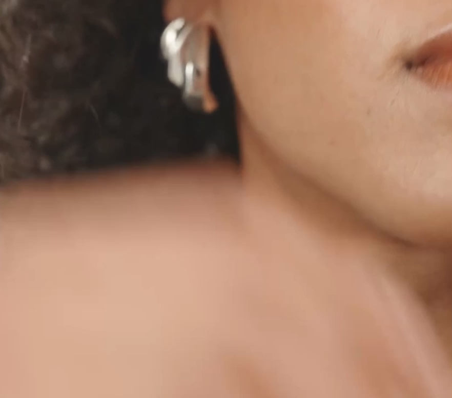 A close-up video of a woman with dark curly hair wearing silver geometric earrings.