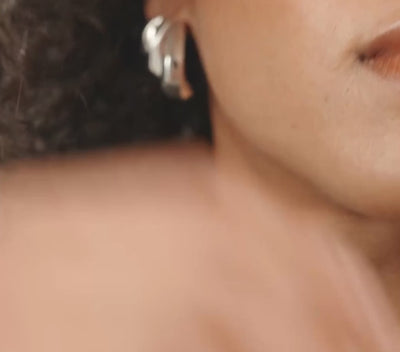 A close-up video of a woman with dark curly hair wearing silver geometric earrings.