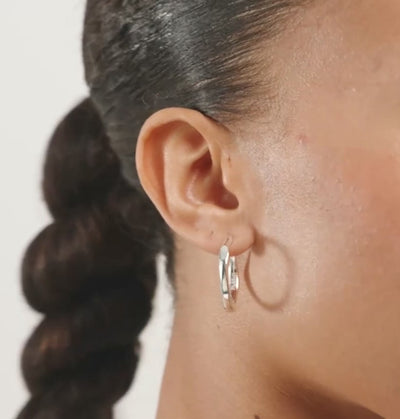A close-up of a model's ear wearing a polished silver-tone hoop earring.