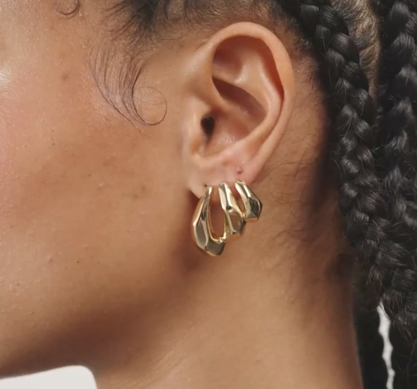 A close-up of a model's ear wearing a pair of gold crescent-shaped hoop earrings.