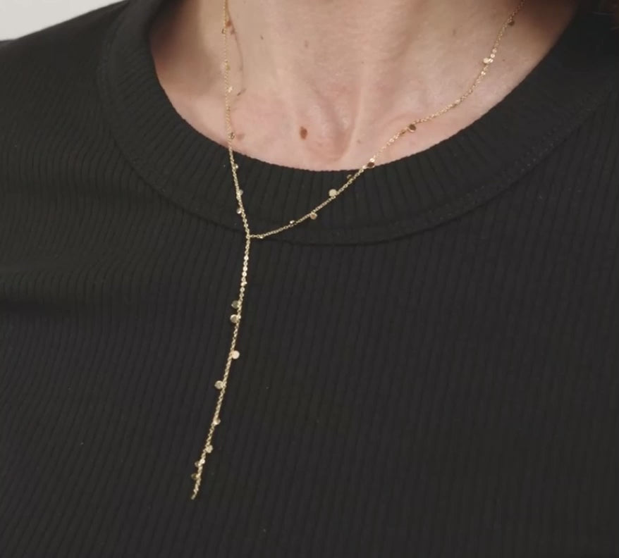 A close-up of a model wearing a delicate gold Y-necklace with tiny dangling charms over a black t-shirt.