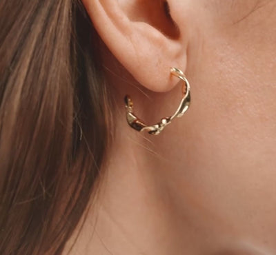 Close-up of a person wearing a gold hoop earring with a plain background