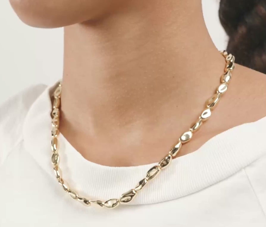 A close-up of a model wearing a polished gold chain necklace with elongated oval links over a white crewneck top.