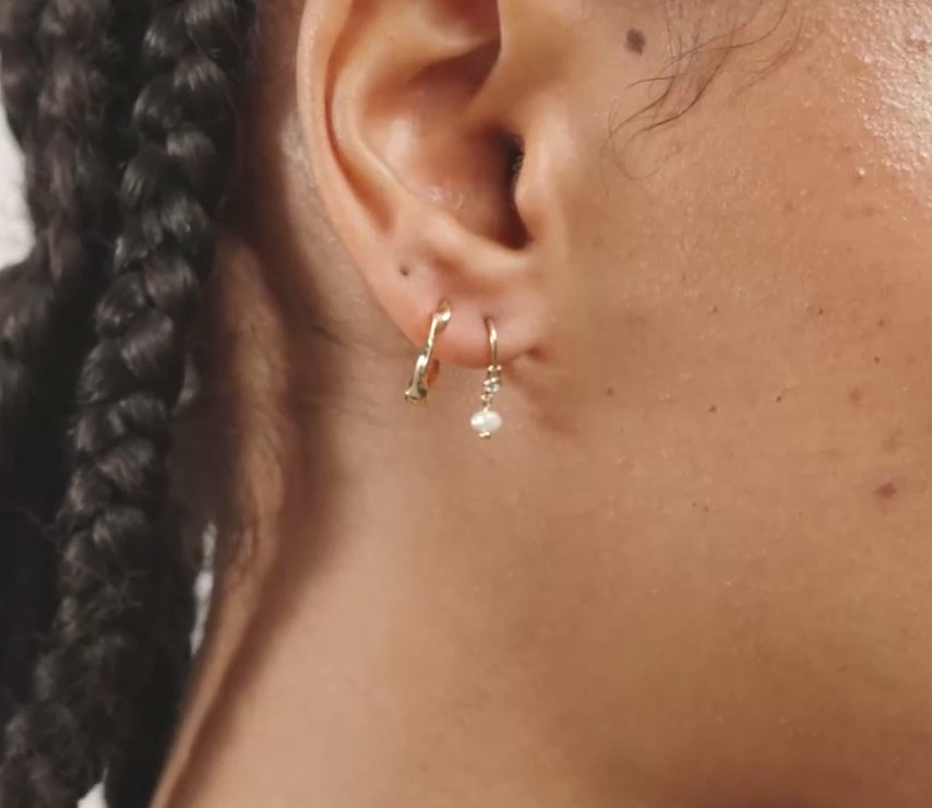 A close-up side profile of a woman's head showing a small gold hoop earring with a tiny clear crystal accent on her earlobe.