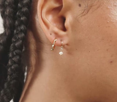 A close-up side profile of a woman's head showing a small gold hoop earring with a tiny clear crystal accent on her earlobe.