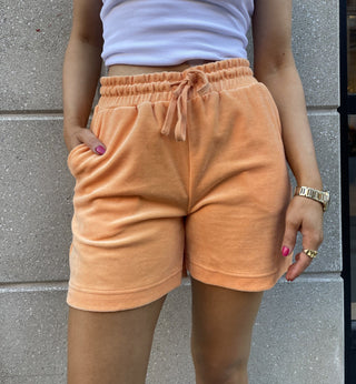 A woman wearing comfy and stylish terry cloth-like sherbet shorts, paired with a white tank top and gold jewelry.